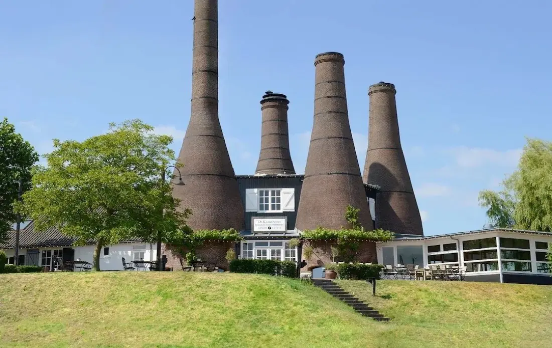 De Kalkovens in Huizen: een wit pand met vier hoge bakstenen kalkovens, op een grasdijk